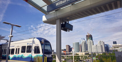 A light rail train arrives at the Wilburton station with downtown in the background.