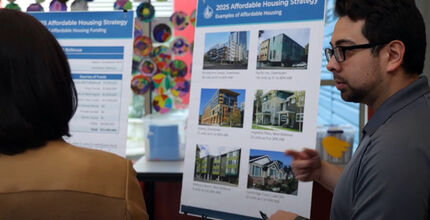 A Bellevue employee explains the city's affordable housing strategy to a woman as he stands by a board showing pictures of housing.