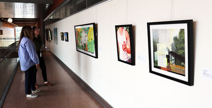 Two women look at paintings hanging in a City Hall corridor.