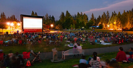 People sit on the grass at Crossroads Park and watch a movie on the big screen.