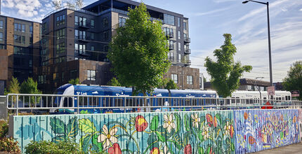 A light rail train passes through BelRed, past a mural and a mid-rise apartment complex. tower.