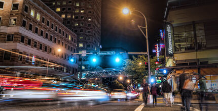 Cars and pedestrians cross an intersection in downtown Bellevue at night.