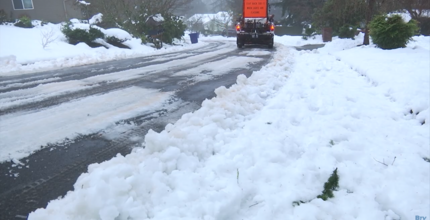 A snow plow truck driving down a curved road with snow build up on either side. 