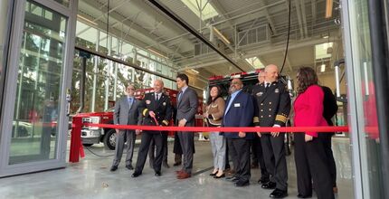 The mayor, deputy mayor and other councilmembers stand with the fire chief behind a red ribbon in the Fire Station 10 bay.