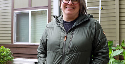 Jenni Treadway of Issaquah stands smiling in front of her new heat pump.