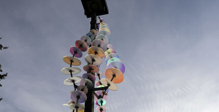 One of the installations that is part of "River" at Crossroads Park features colored glass disks threaded on metal wires draped around a light pole. lass