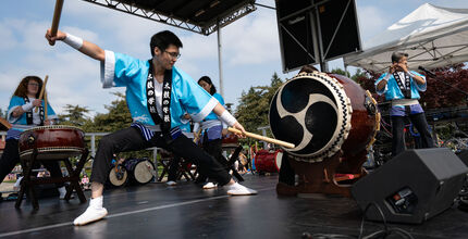 A man strikes a big taiko drum on a stage.
