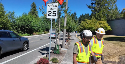 Workers walk away from a 25-mph speed limit sign they just installed by a Bellevue streeet.