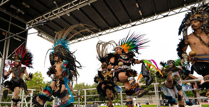 Danza Azteca performers dance in Aztec costumes on a stage at Crossroads Park.