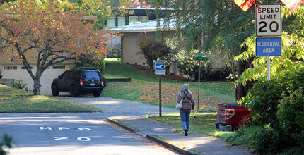 A woman walks on a sidewalk in the Surrey Downs neighborhood, past a sign advertising 20-mph speed limit.