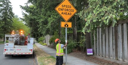 A Transportation worker installs a sign next to a street that reads "speed enforced ahead."