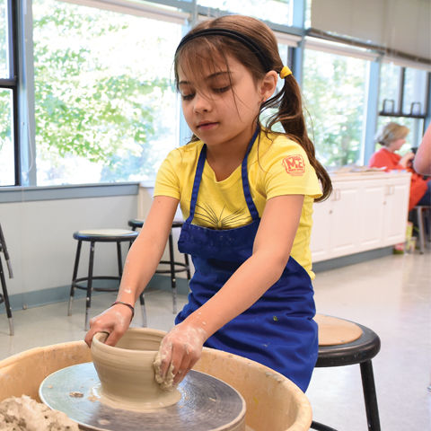 girl in a yellow top and blue skirt doing pottery