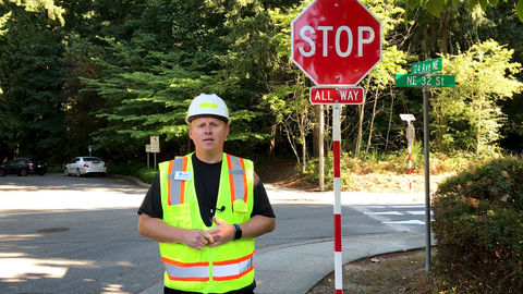 A city worker stands in front of a stop sign and street sign on a residential street