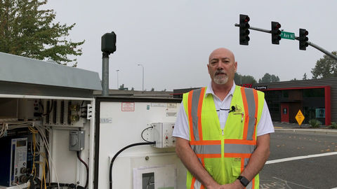 A city worker stands in front of a traffic signal control cabinet at an intersection