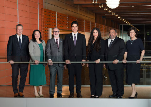 Seven men and women, members of the City Council, stand in a hallway at City Hall.