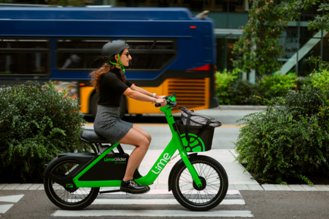 Woman rides a Lime glider in a bike lane with a blue bus in the background