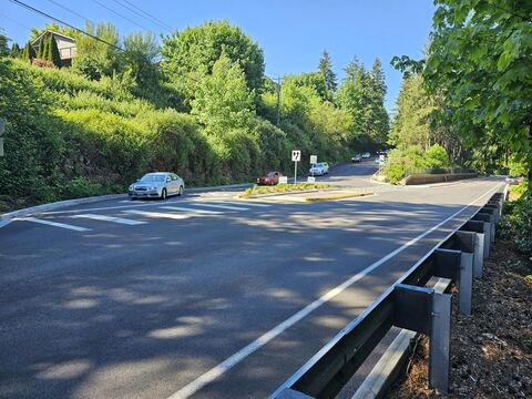 Two line road with a crosswalk in the distance and a guardrail with a shoulder