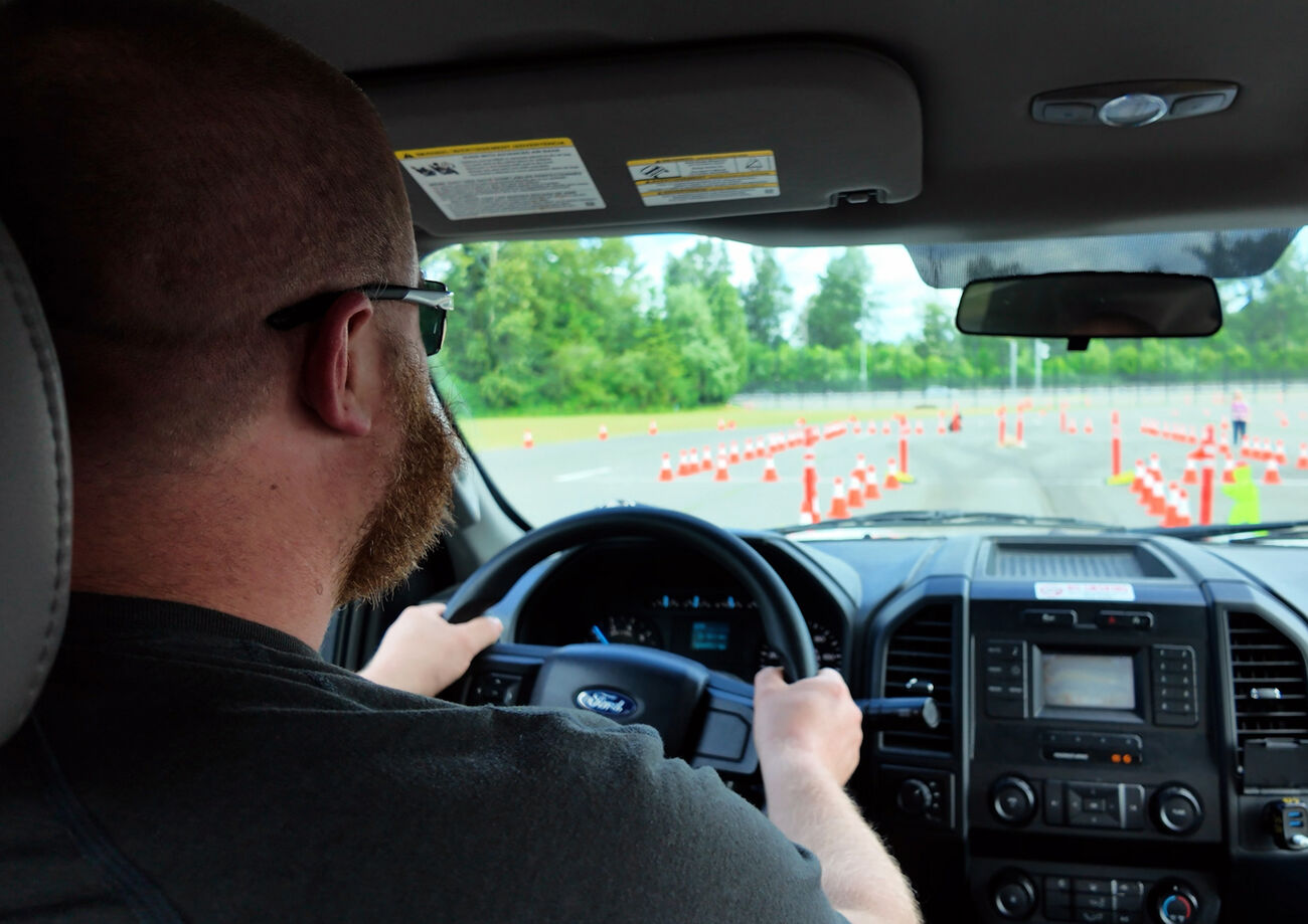 A man drives a truck on a parking lot with cones laid out in rows.