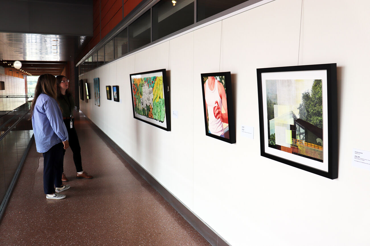 Two women look at paintings hanging in a City Hall corridor.