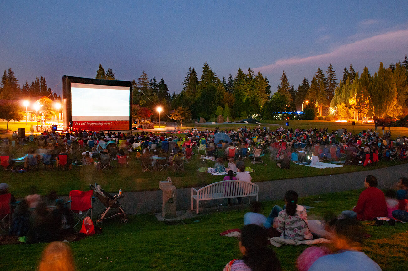 People sit on the grass at Crossroads Park and watch a movie on the big screen.