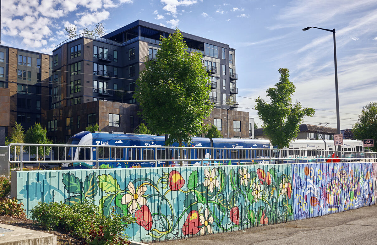 A light rail train passes through BelRed, past a mural and a mid-rise apartment complex. tower.