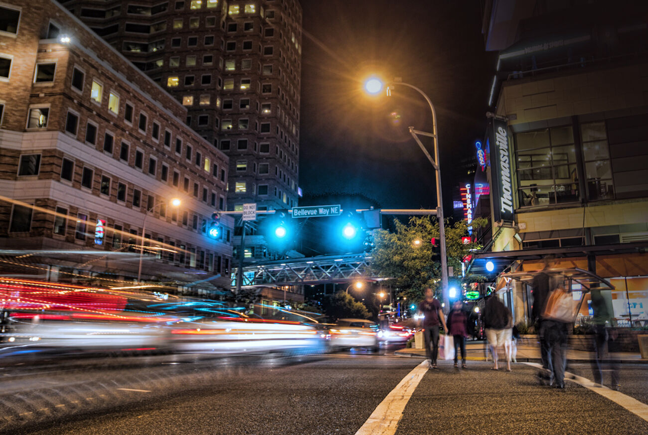 Cars and pedestrians cross an intersection in downtown Bellevue at night.