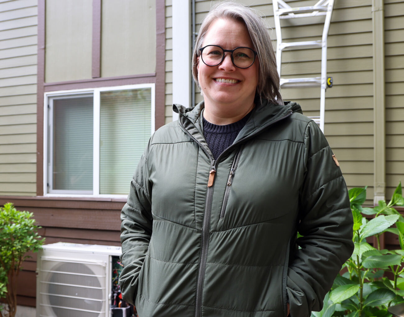 Jenni Treadway of Issaquah stands smiling in front of her new heat pump.
