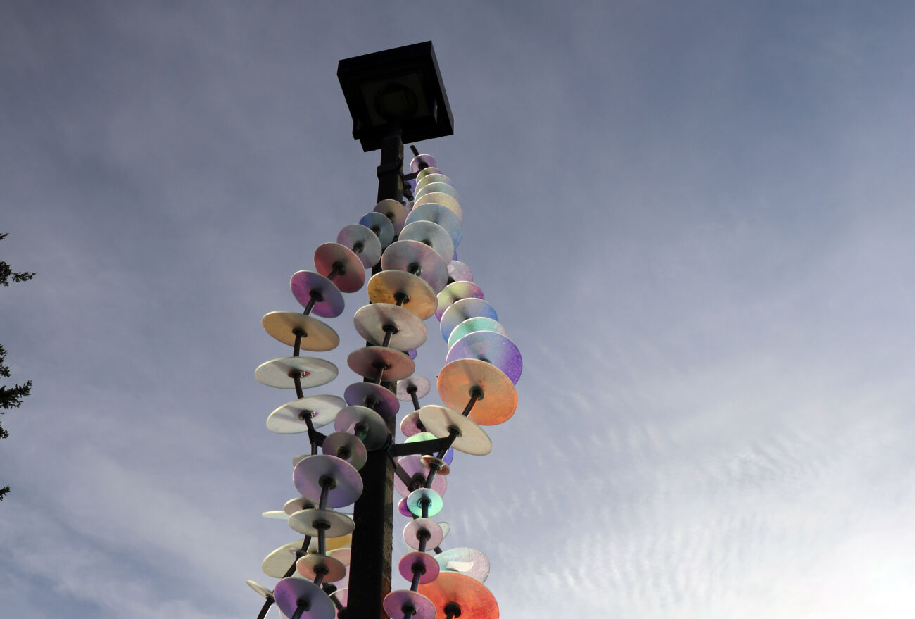 One of the installations that is part of "River" at Crossroads Park features colored glass disks threaded on metal wires draped around a light pole. lass