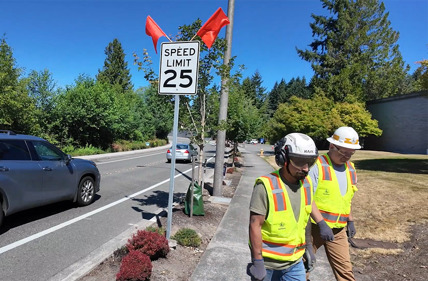 Workers walk away from a 25-mph speed limit sign they just installed by a Bellevue streeet.