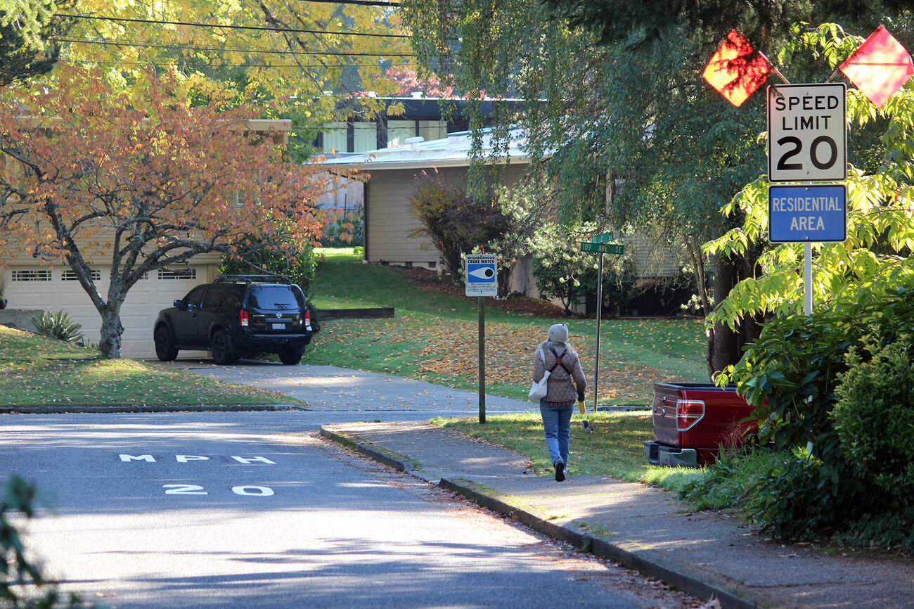 A woman walks on a sidewalk in the Surrey Downs neighborhood, past a sign advertising 20-mph speed limit.