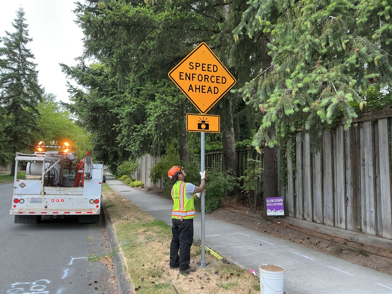 A Transportation worker installs a sign next to a street that reads "speed enforced ahead."