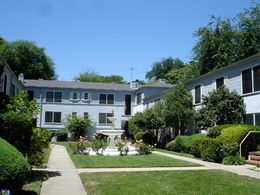 The photo shows an apartment building with two floors arranged around a courtyard with grass, pathways and a fountain. 