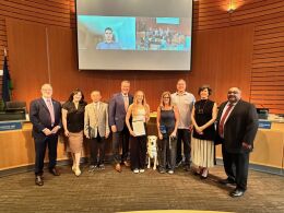 A service dog and others pose with the City Council in the council chamber.