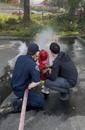 A Bellevue Firefighter helps a young boy hold a fire hose. 