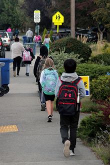 Children wearing backpacks facing away from the camera and walking along a sidewalk