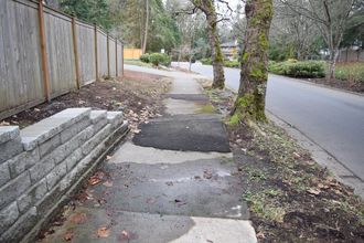 A photograph of a ramped sidewalk that has been patched with asphalt.