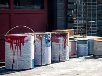 Image of used paint cans outside by a garage.