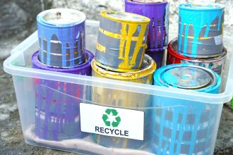 Image of used cans of paint in a large clear tub with a recycle sticker on it.