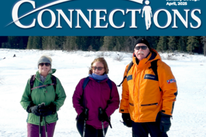 image of three people, smiling at camera. They are outdoors in a snowy meadow, wearing winter coats and holding snowshoeing poles. 