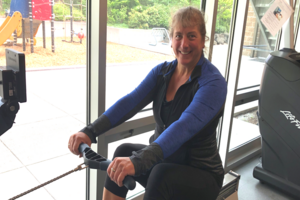 An image of a woman using a rowing machine in a well-lit Fitness Center with glass windows in the background.