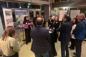 A group of people listens to a speaker presenting information about Digital Equity.