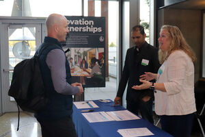 Three people converse at an information table.