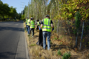 Volunteers in neon safety vests pick up litter along a city street.