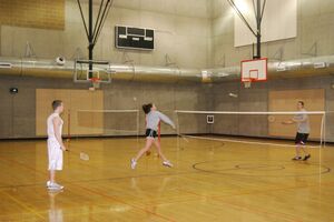 three people playing badminton at an indoor court