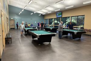 multiple groups of people in a game room playing pool 