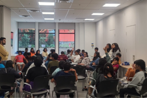 People in a classroom, one person has their hand raised