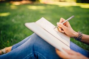 a person sits outside and writes in a notebook