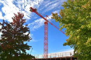 A construction crane is visible over a building under construction. Trees frame the crane.