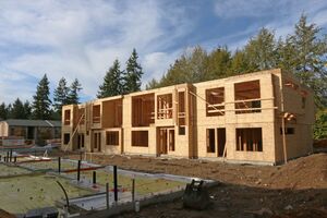 A building under construction. In the foreground another building foundation is visible. Trees are in the background.
